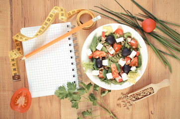 Vintage photo, greek salad with vegetables, centimeter and notepad for notes, healthy nutrition and slimming concept