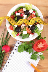Fresh greek salad with vegetables, centimeter and notepad for writing notes, healthy nutrition and slimming concept