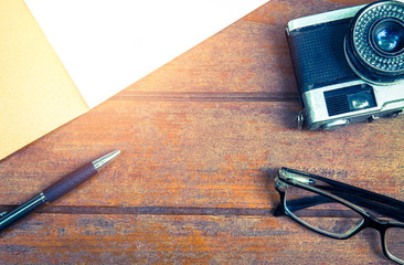 Overview wooden desk of creative,designer with notebook,glasses,pen and camera (vintage filter)