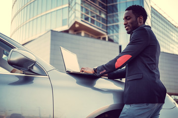 Fototapeta premium Stylish african male using laptop near his car.