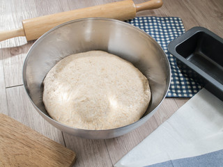 bread dough in stainless steel bowl and baking utensils on wooden background