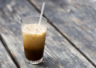 Cold coffee with milk in a glass beaker. Cold drink with ice on a wooden table. 