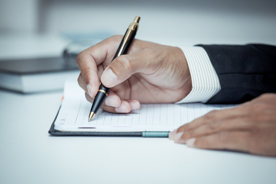 Businessman writing on notebook with pen in the office in blue c