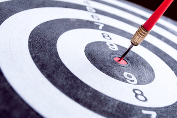 Red dart arrow hitting in the target center of dartboard