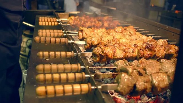 Grilled meat on skewers. Street food. Meat rotating on skewer. Food grilling on barbecue. Preparing tasty meat barbeque on skewers. Shashlik grill over coals. Grilled meat shashlik. Shish kebab.