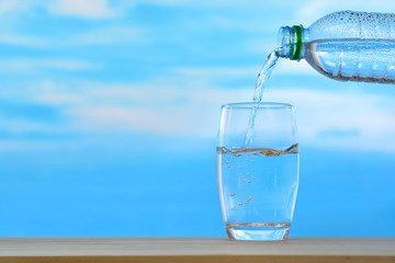 Fresh and clean drinking water being poured from bottle into glass on sky background