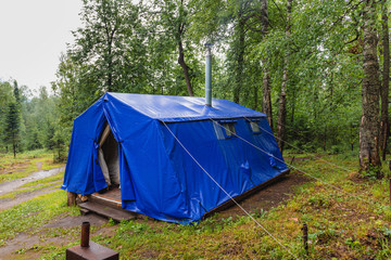 Military tent with stove and chimney pipe in a summer forest