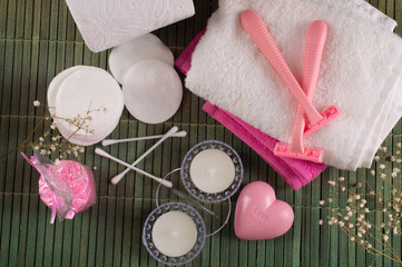 Set for SPA: cotton swabs, razors, cotton pads, towels, napkins, bath salt on a green bamboo background flat lay.