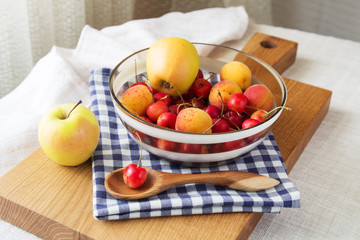 Composition of fruits and berries. Reason for the longevity is apples, cherries, apricots. Fruits and berries in a bowl on a checkered napkin on the table. Fruits and berries on a wooden cutting board