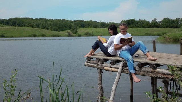 man and woman reading and discussing  books on the board table near lake. 4K stock footage clip.
