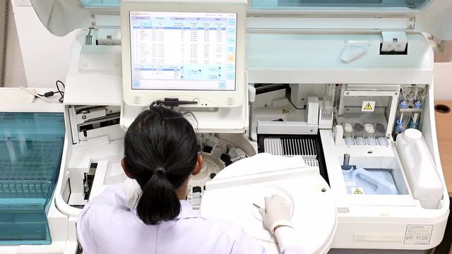 Woman working in laboratory on modern machine for blood testing. Medical staff works machine with display for control blood. Doctor at hospital checked sample in machine above view. Analysis of blood.