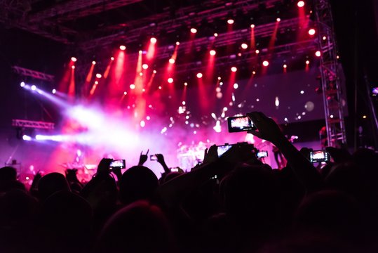 Rock concert, silhouettes of happy people raising up hands in front of bright stage lights