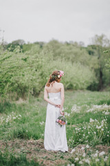 Fototapeta na wymiar Beautiful bride in a wedding dress with bouquet and roses wreath posing in a green garden. Wedding day