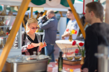 Beautiful blonde caucasian lady buying freshly prepared meal at a local street food festival. Urban...