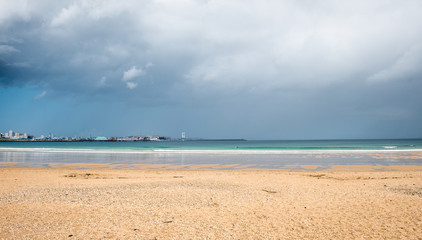 Tropical sandy beach with storm clouds and city in background.