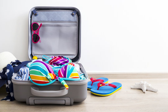 Colorful bikini and clothes in luggage on the laminate floor