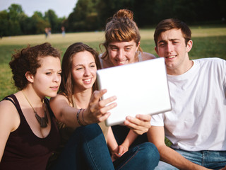 large group of friends tohether in a park using a tablet