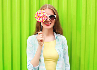 Portrait happy pretty smiling woman and lollipop over colorful g