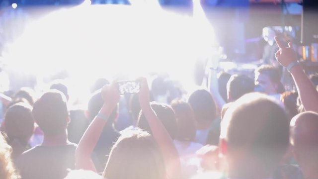 girl capturing a concert with a smartphone, large group of happy people enjoying rock concert, clapping with raised up hands, lights from the stage 4