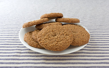 Oatmeal sugar free cookies on a white plate atop a blue striped tablecloth.