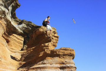 Man with backpack standing on top of mountain and looking at fly seagull