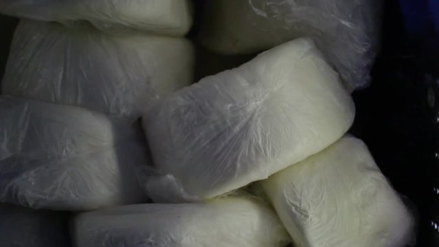 Cheese heads wrapped in cellophane. Farm product in dairy shop. Hard cheeses. Cheese heads on shelves. Dairy products in cheese shop. White cheese at dairy farm. Stack of cheese heads in package