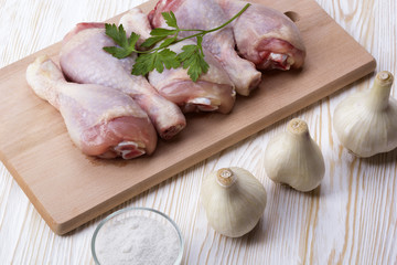 raw chicken drumstick on the board with salt, garlic, parsley