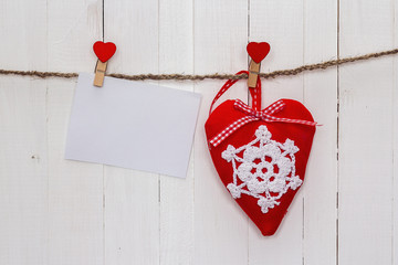 White blank paper card with heart hanging on white wooden painte