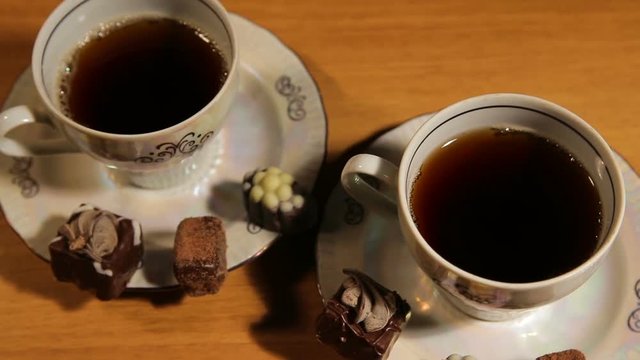 Chocolate candies and tea set on a wooden table.Cup of hot blak tea with chocolate candy.Porcelain tea set on an black background.Two teacups and teapot.Vintage tea set for two persons.