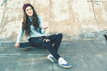 Hipster skateboarder girl with skateboard outdoor sitting at skatepark