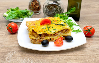 Appetizing lasagna with tomato and olives on a plate.