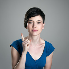 Smiling young short hair woman scolding finger looking at camera over gray studio background 