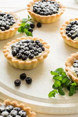 Close up of tartlets with fresh blueberries, decorated mint leaves on white wooden background. Selective focus