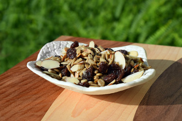 White handmade clay dish filled with trail mix with sliced almonds, salted sunflower kernels, and sugared raisins on a handmade wood cutting board