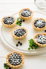Close up of tartlets with fresh blueberries, decorated mint leaves on white wooden background. Selective focus
