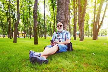 Obraz premium Aged stylish man sitting under the tree and listening to music