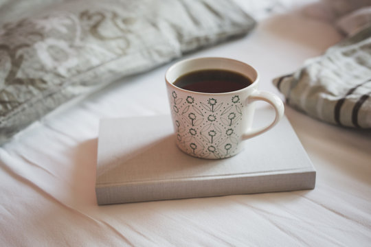 Book and cup of black coffee on a bed
