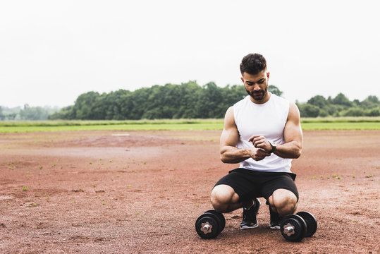 Athlete crouching with dumbbells on sports field