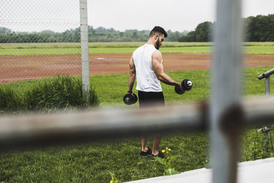 Athlete exercising with dumbbells on sports field