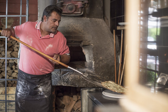 Pizza baker with pizza on pizza peel, pizza oven