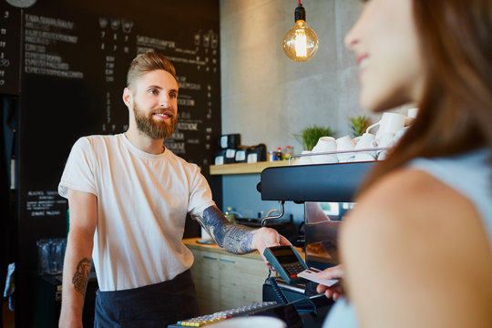 Happy barista giving payment terminal to client at modern cafe