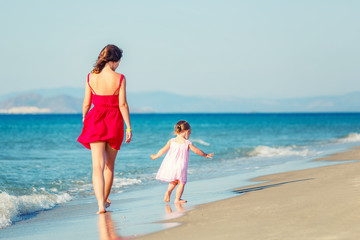 Mother and little daughter walking on the beach