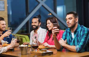 man with smartphone and friends at restaurant