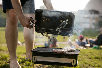 Mann wendet Burger mit Grillzange im Park