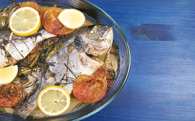 Baked fish with carrot,lemon and greenery.From above. The wooden table is blue.