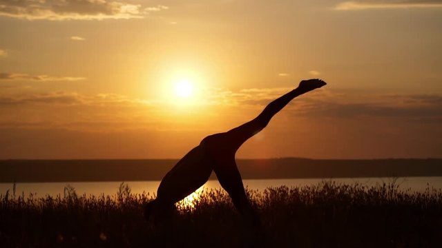 Silhouette of young sportive man practicing yoga at sunset. Slow motion.