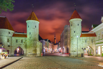 Fototapeta premium Guard towers of Viru Gate, Narrow street illuminated of Old Town at night, City Hall on the background, Tallinn, Estonia