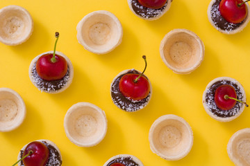 Delicious chocolate tartlets with one cherry, chocolate and coconut on yellow background

