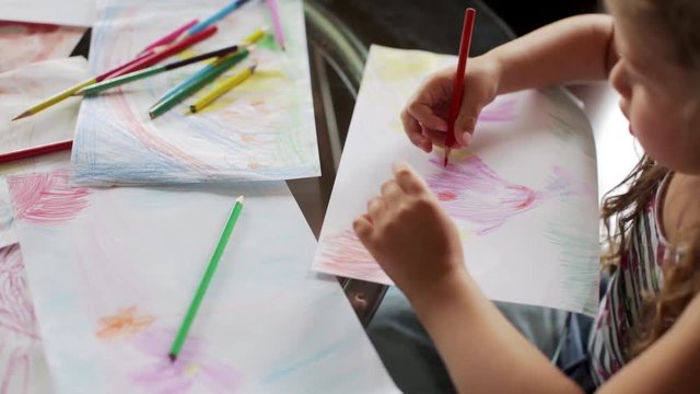 little girl draws with crayons sitting at table. close up