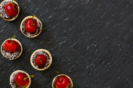 Delicious chocolate tartlets with one cherry, chocolate and coconut on slate background

